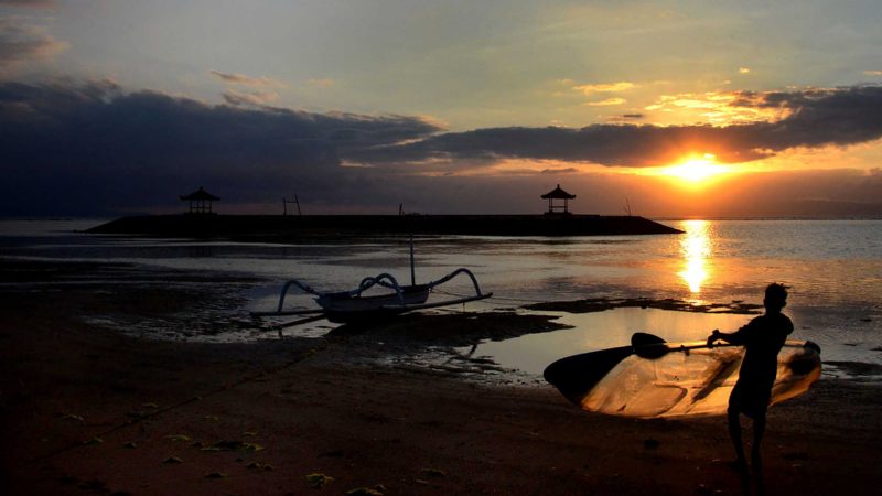 A man carries a canoe during sunrise at a beach in Sanur on Indonesia's resort island of Bali on September 28, 2021. (Photo by SONNY TUMBELAKA / AFP)