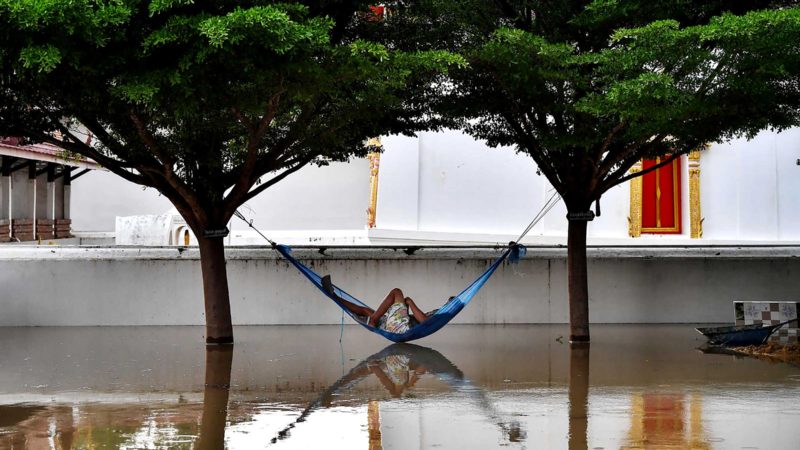 A man rests in a hammock in the grounds of a flooded Buddhist temple in the central Thai province of Ayutthaya on September 28, 2021, as tropical storm Dianmu caused flooding in 30 provinces across the country. (Photo by Lillian SUWANRUMPHA / AFP)