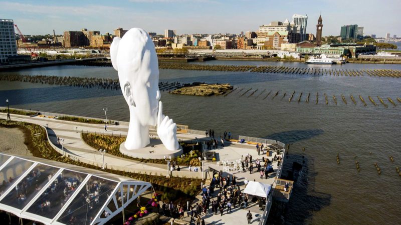 City officials and developers dedicated a permanent new sculpture titled "Water's Soul" on Thursday, Oct. 21, 2021, in Jersey City, N.J. The 80-foot tall sculpture depicts a young woman with a finger on her lips shushing or calling for silence from the New York City skyline across the Hudson River. Artist Jaume Plensa from Barcelona, Spain, says he intends the sculpture to inspire silent contemplation. (AP Photo/Ted Shaffrey)