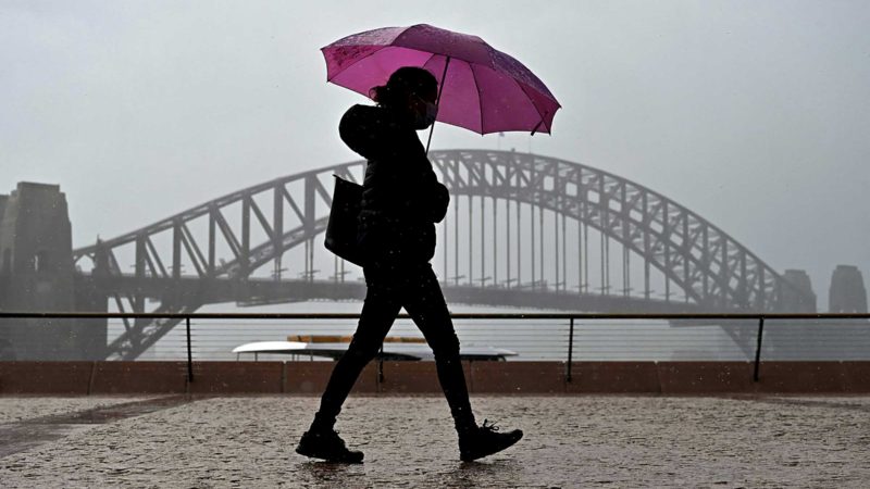 A woman holding an umbrella walks past the Sydney Harbour Bridge in Sydney on October 10, 2021, a day before the expected easing of coronavirus restrictions in Australia's largest city. (Photo by Steven Saphore / AFP)