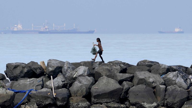 A boy holds his day's catch of crabs as he walks along the breakwater in Manila, Philippines on Saturday, Sept. 25, 2021. (AP Photo/Aaron Favila)