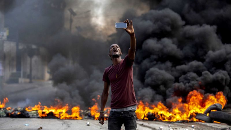 A protester takes a selfie at a burning barricade set by protesters in Port-au-Prince, Haiti, Monday, Oct. 18, 2021. Workers angry about the nation’s lack of security went on strike in protest two days after 17 members of a U.S.-based missionary group were abducted by a violent gang. (AP Photo/Joseph Odelyn)