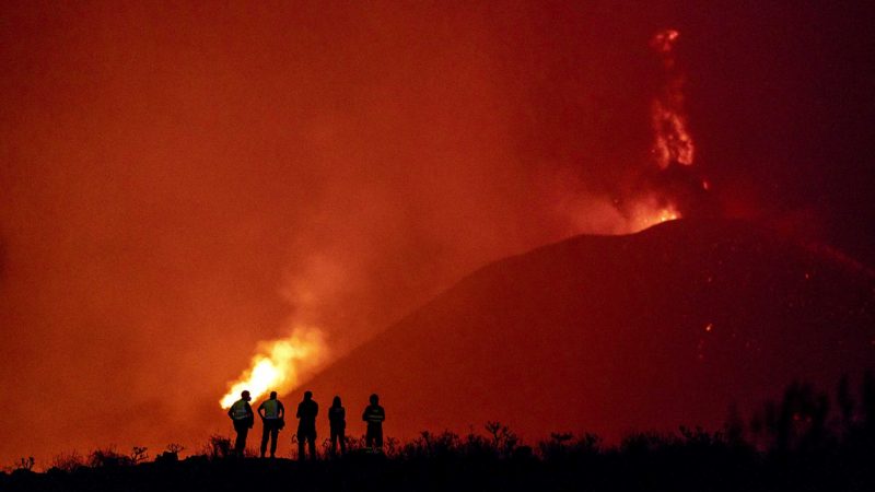 Police officers and emergency personnel look as lava flows from a volcano as it continues to erupt on the Canary island of La Palma, Spain, Tuesday, Nov. 2, 2021. A volcano on the Spanish island of La Palma that has been erupting for six weeks has spewed more ash from its main mouth a day after producing its strongest earthquake to date. (AP Photo/Emilio Morenatti)
