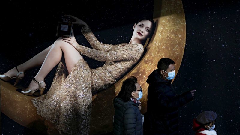 Shoppers wearing face masks to help curb the spread of the coronavirus walk by a perfume advertisement billboard on display at a capital popular shopping mall in Beijing, Monday, Nov. 8, 2021. (AP Photo/Andy Wong)